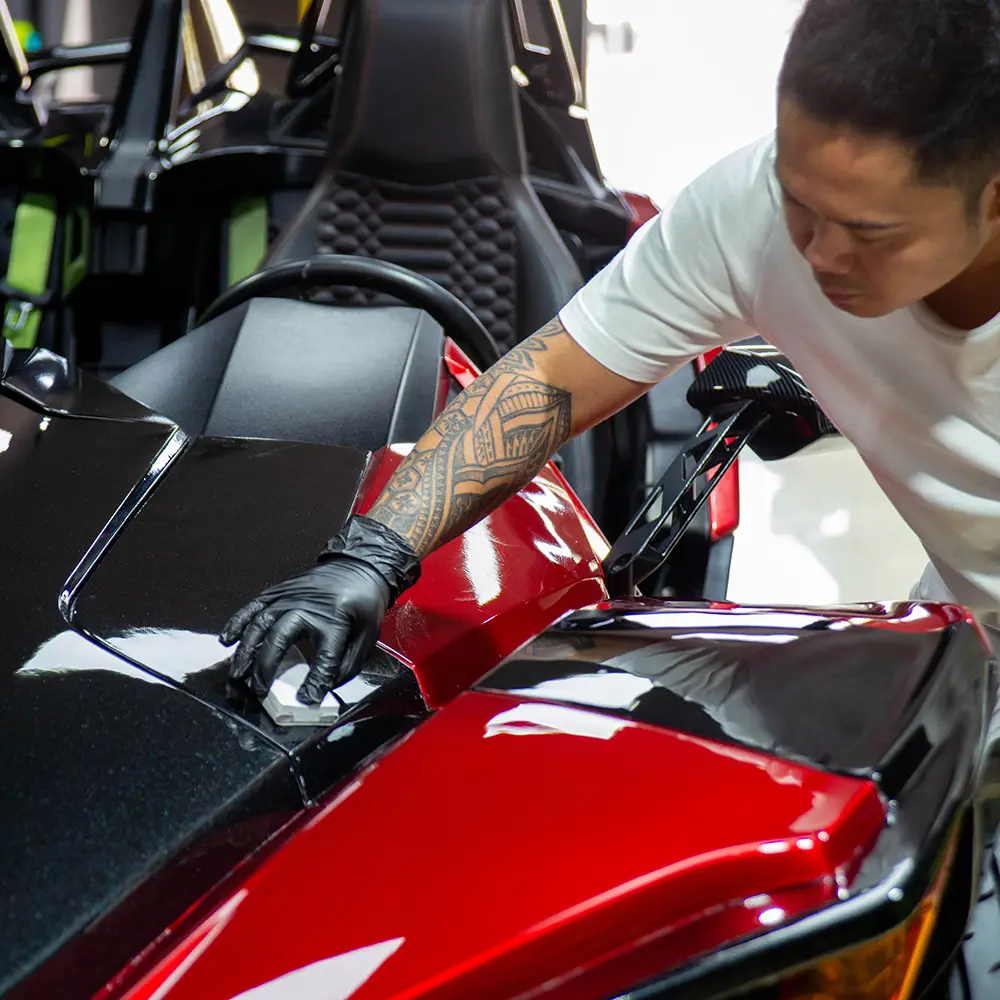 Expert technician performing ceramic coating application on a black and red Polaris Slingshot to enhance gloss and surface protection.